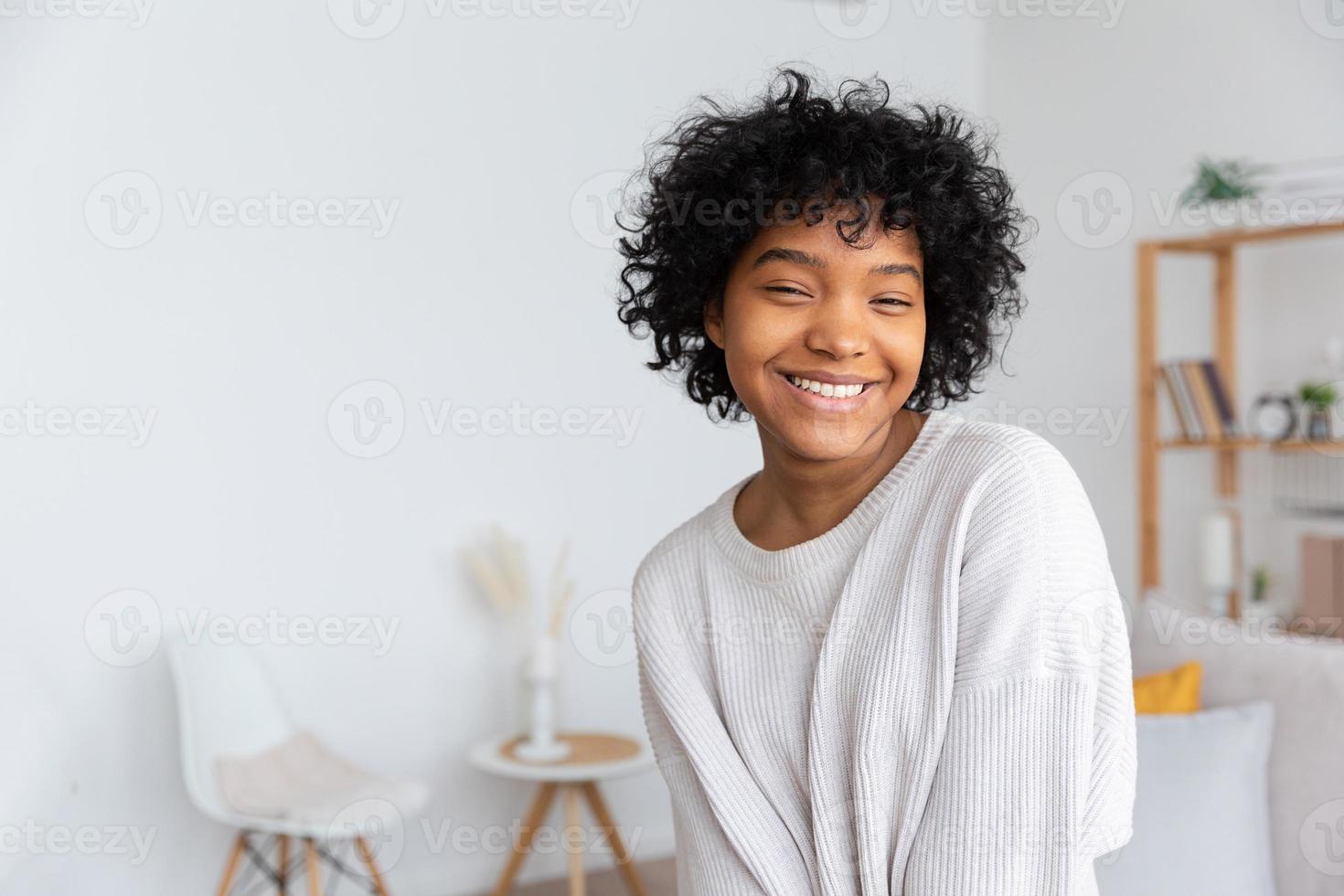 mooi Afrikaanse Amerikaans meisje met afro kapsel glimlachen Bij huis binnen. jong Afrikaanse vrouw met gekruld haar- lachend in leven kamer. vrijheid geluk zorgeloos gelukkig mensen concept. foto