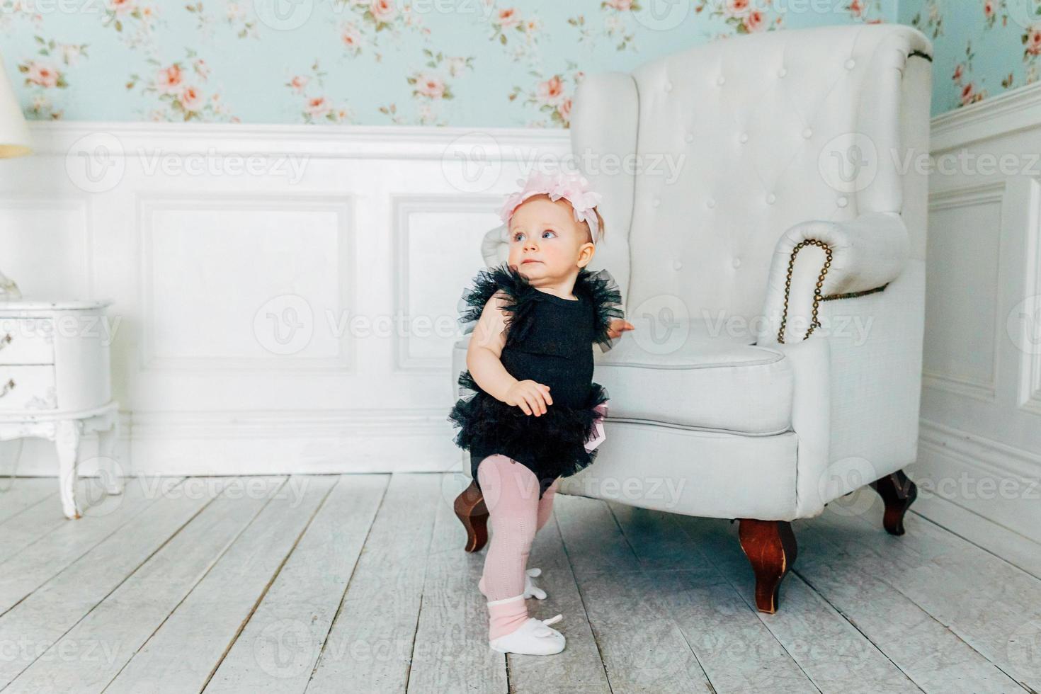 weinig baby meisje staand in de buurt stoel in helder licht leven kamer glimlachen en lachend foto