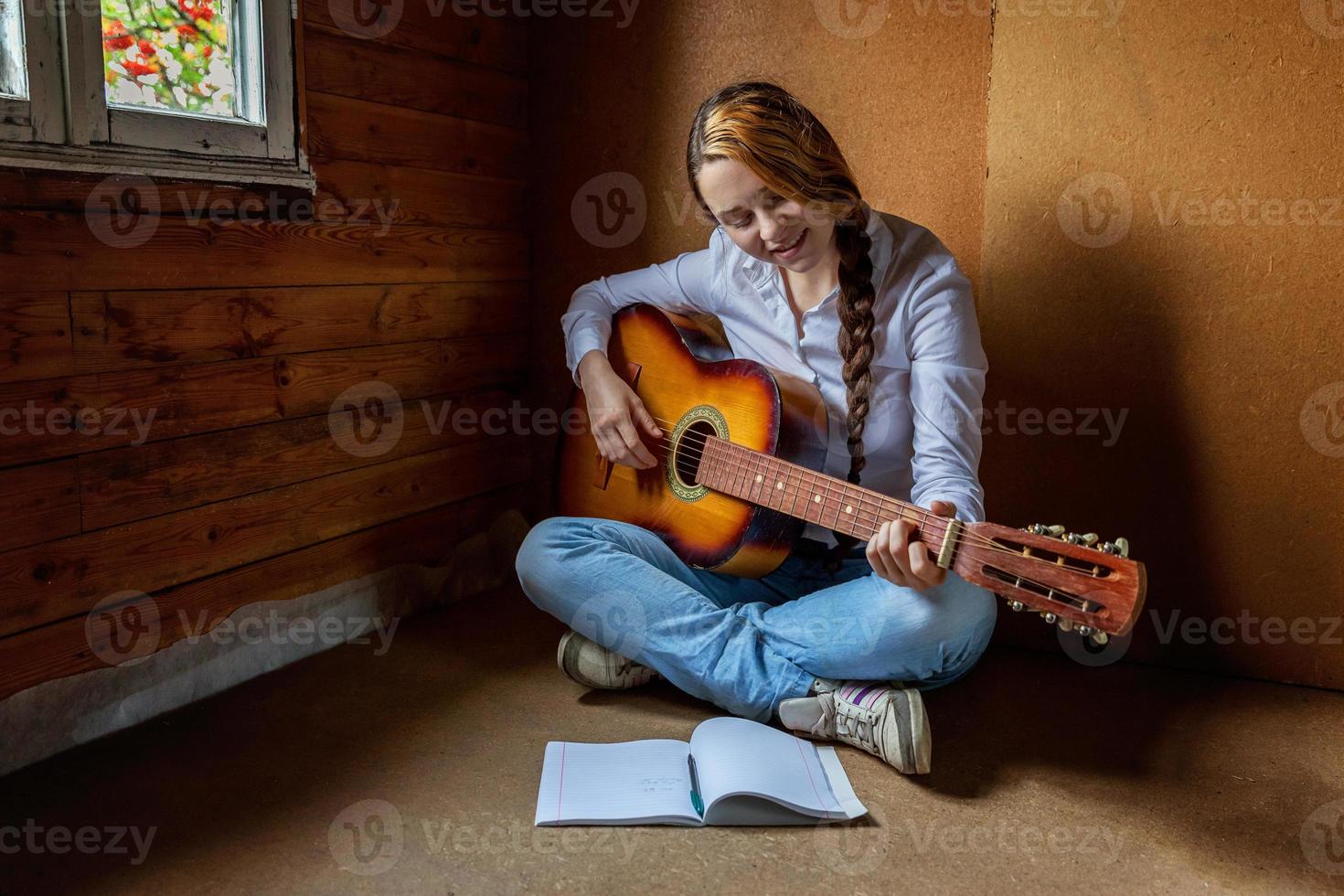 jong hipster vrouw zittend Aan verdieping en spelen gitaar Bij huis. tiener meisje aan het leren naar Speel lied en schrijven muziek- in haar kamer. hobby, levensstijl, kom tot rust, instrument, vrije tijd, onderwijs concept. foto