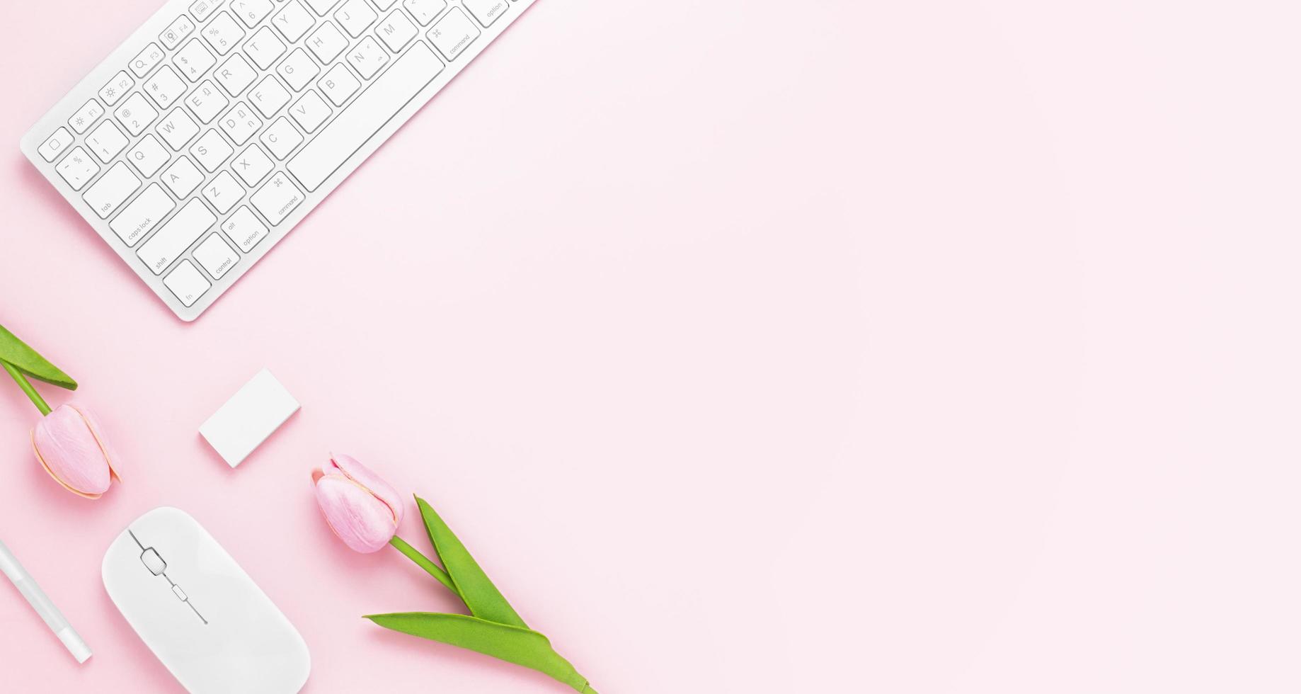minimale bureautafel met toetsenbordcomputer, muis, witte pen, tulp bloemen, gum op een roze pasteltafel met kopie ruimte voor het invoeren van uw tekst, roze kleur werkplekcompositie, plat leggen, bovenaanzicht foto