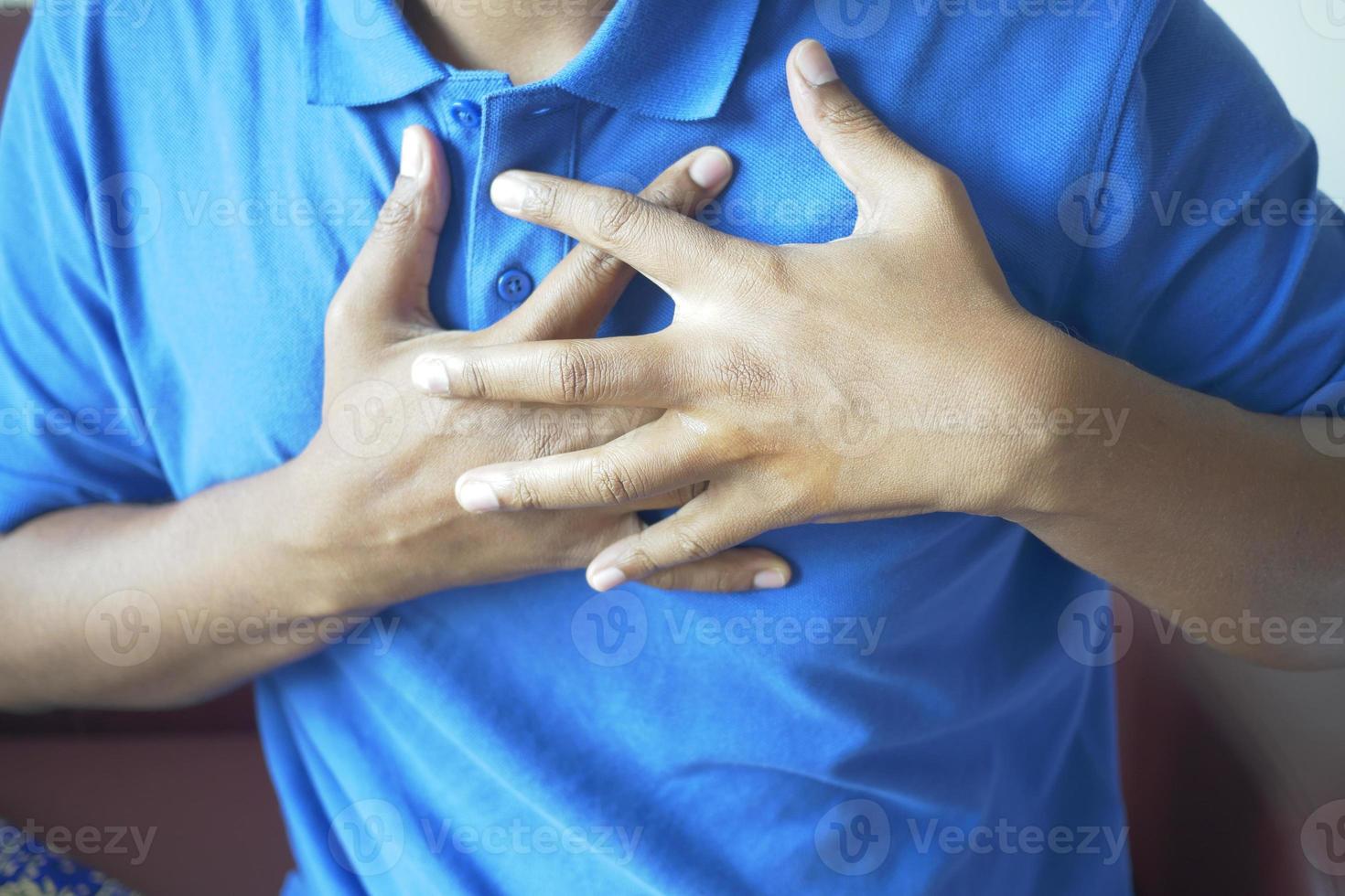 jonge man die pijn in het hart lijdt en de borst met de hand vasthoudt foto