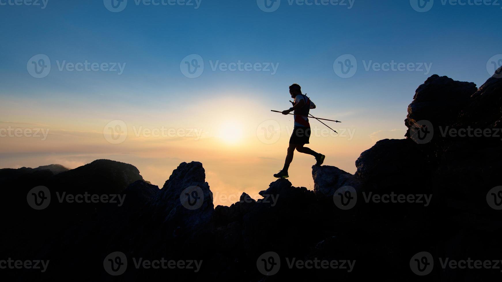 zonsondergang silhouet van skyrunner Mens aflopend van alpine nok met polen foto