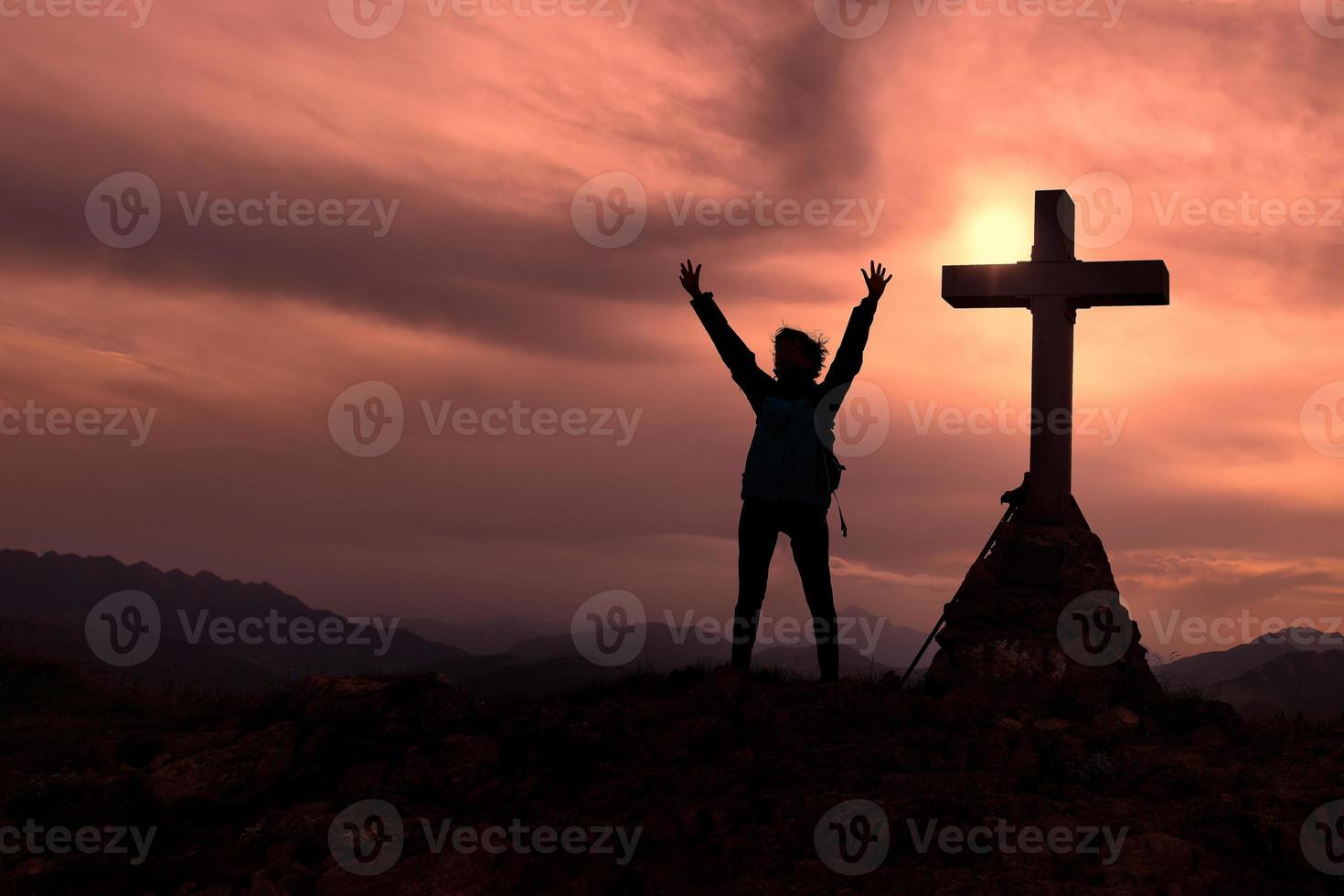 kruis Bij de top van de berg met een bergbeklimmer wie verhoogt zijn handen foto