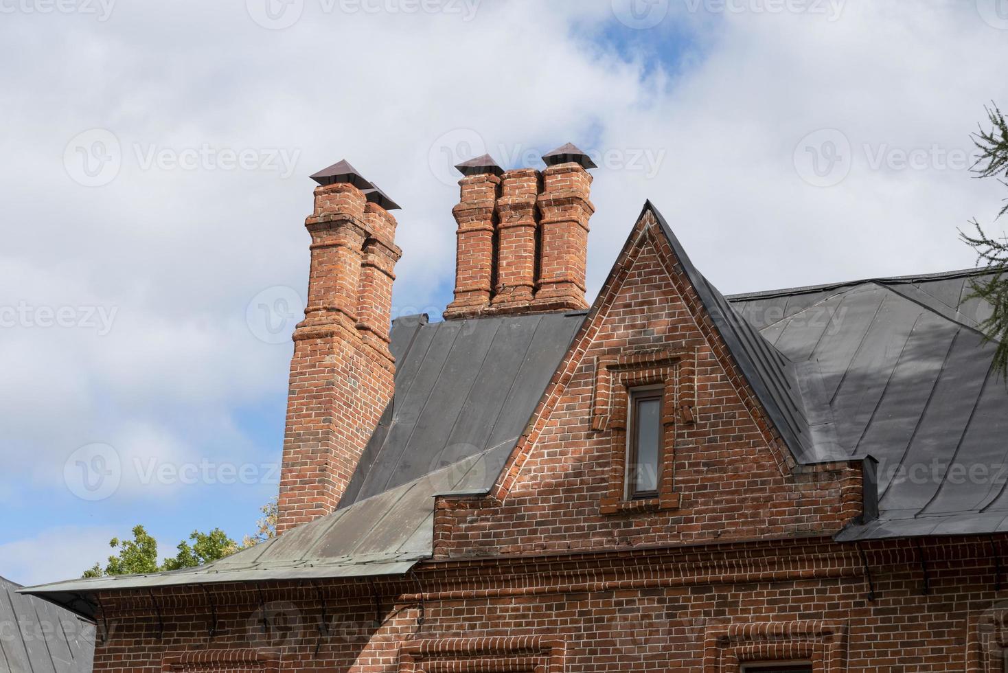 rood dak tegels met een rood steen schoorsteen Aan een blauw lucht achtergrond. foto