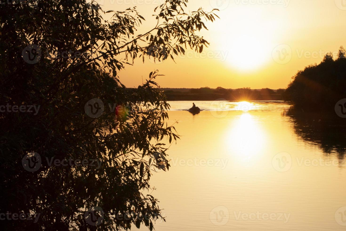 zonsondergang Aan de meer tussen de bomen en in de afstand een boot met een visser. foto