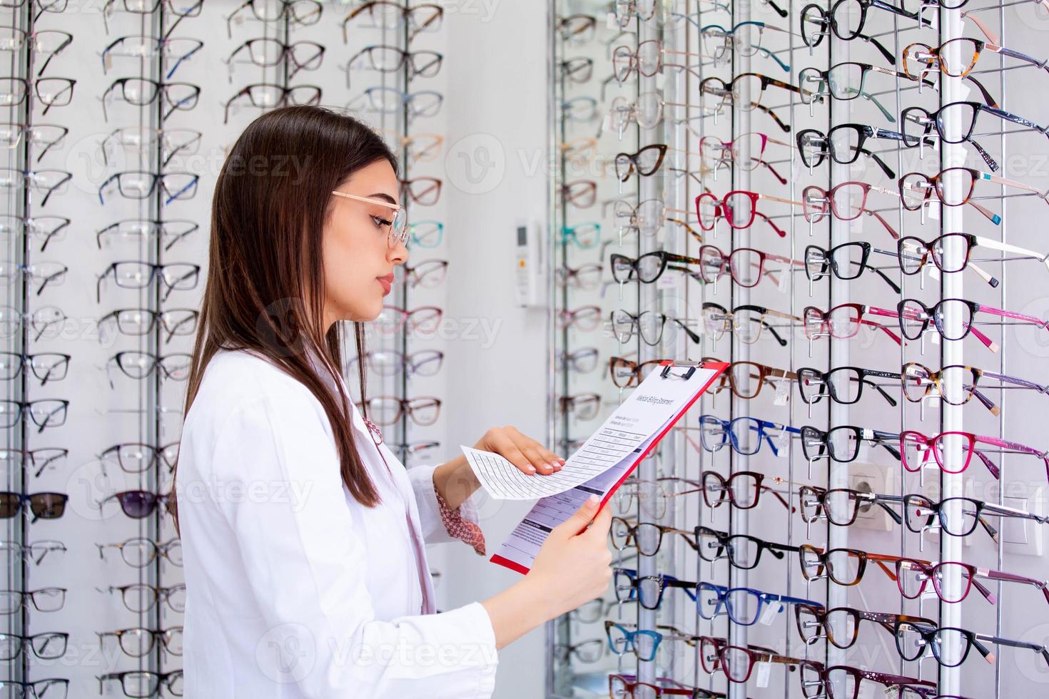 aantrekkelijk vrouw oogarts schrijven gegevens naar een klembord, werken in een optisch op te slaan. gezondheidszorg en geneeskunde concept foto