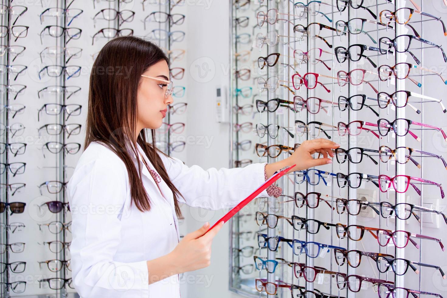 aantrekkelijk vrouw oogarts schrijven gegevens naar een klembord, werken in een optisch op te slaan. gezondheidszorg en geneeskunde concept foto