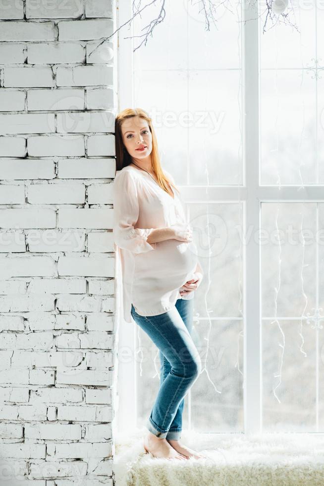 roodharig zwanger meisje in een licht blouse en blauw jeans foto