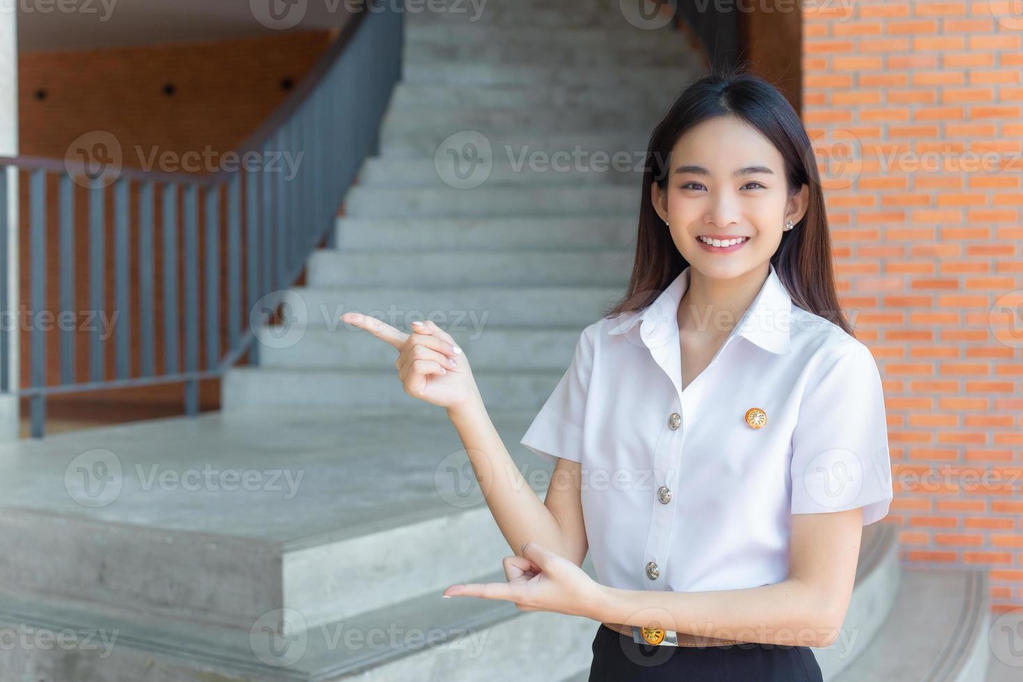 schattig Aziatisch jong vrouw leerling is glimlachen en op zoek Bij camera staand naar Cadeau iets vol vertrouwen in Universiteit achtergrond. foto