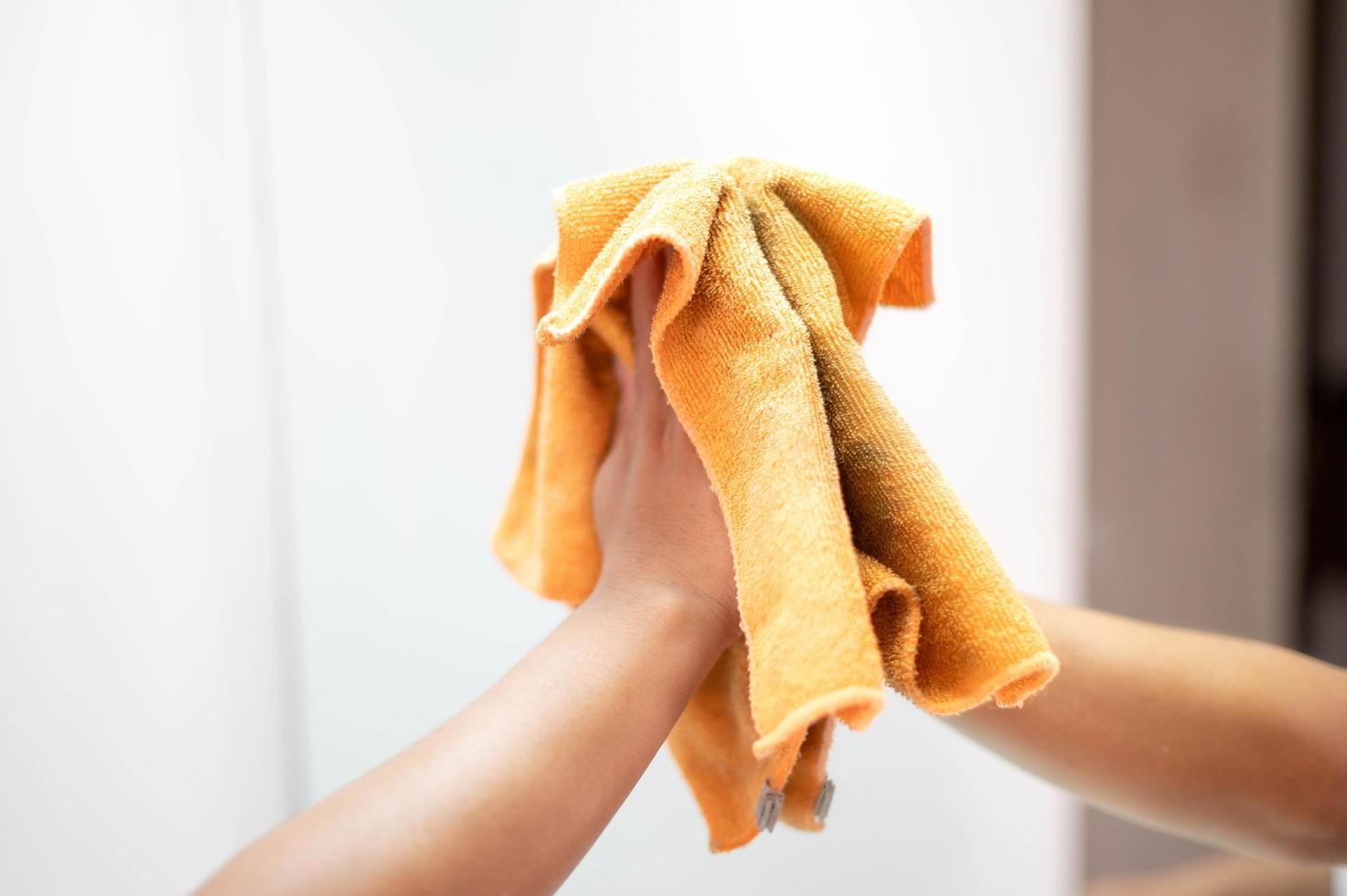 vrouw hand- schoonmaak en afvegen de spiegel met oranje microfiber kleding in de leven kamer. huishouding concept. foto