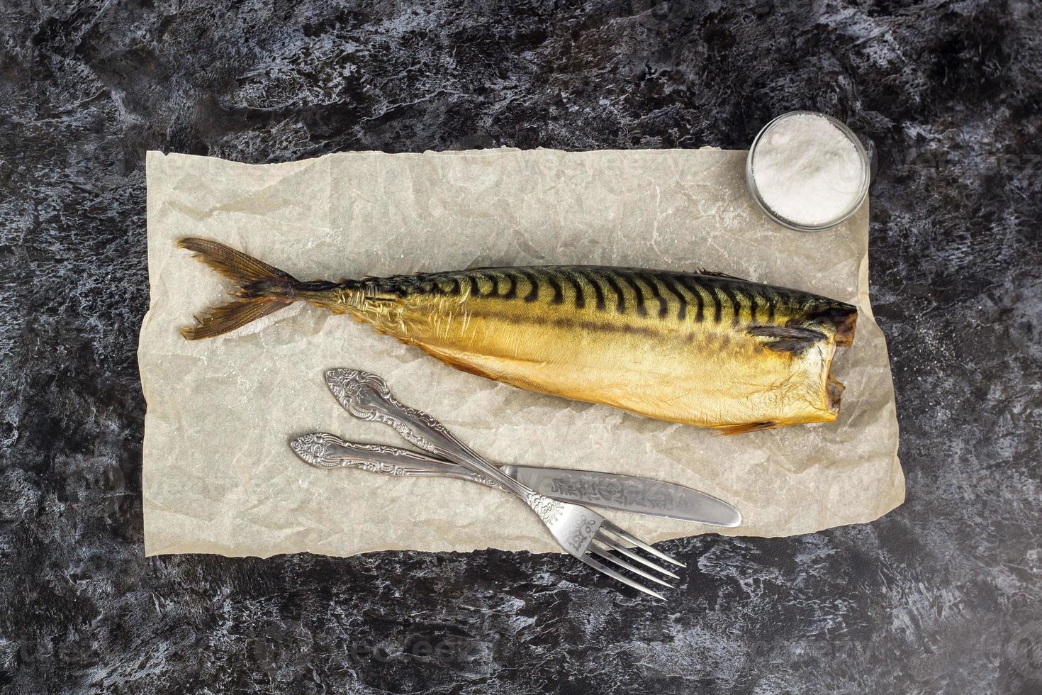 gerookt makreel zonder hoofd met vork mes Aan bakken papier Aan zwart achtergrond foto