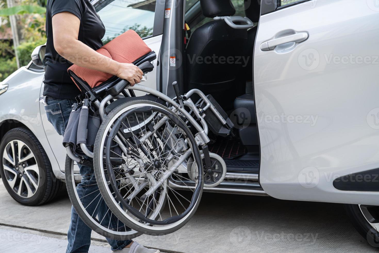 aziatische vrouw vouwt en tilt rolstoel op in haar auto. toegankelijkheidsconcept. foto