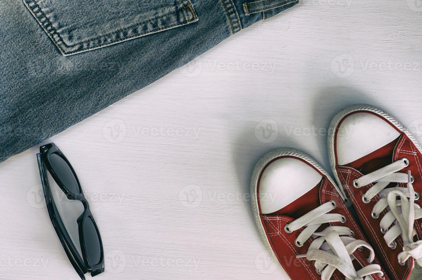 paar- van rood sportschoenen, retro fragment jeans, zwart zonnebril Aan een wit houten achtergrond foto