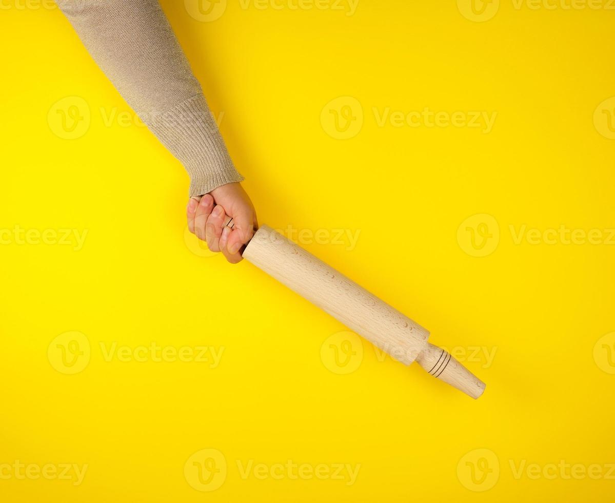 hand- Holding een houten rollend pin Aan een geel achtergrond foto