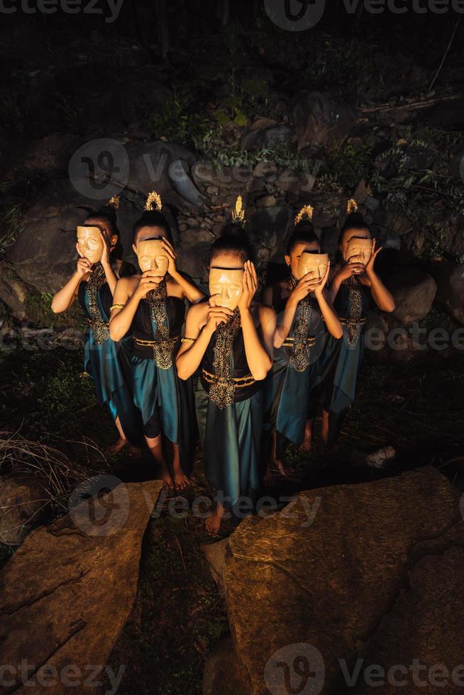 een groep van Aziatisch Dames vervelend een houten maskers in groen kostuums terwijl staand tussen de rotsen binnen de Woud foto