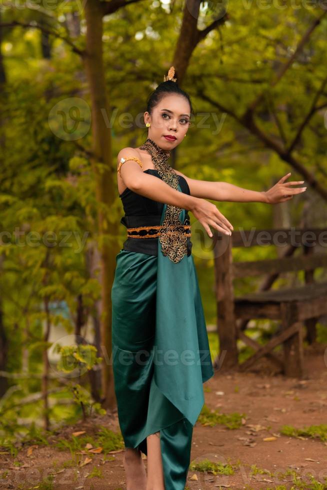 Javaans vrouw dansen in voorkant van de bossen in groen kostuum terwijl in bedenken en het uitvoeren van foto