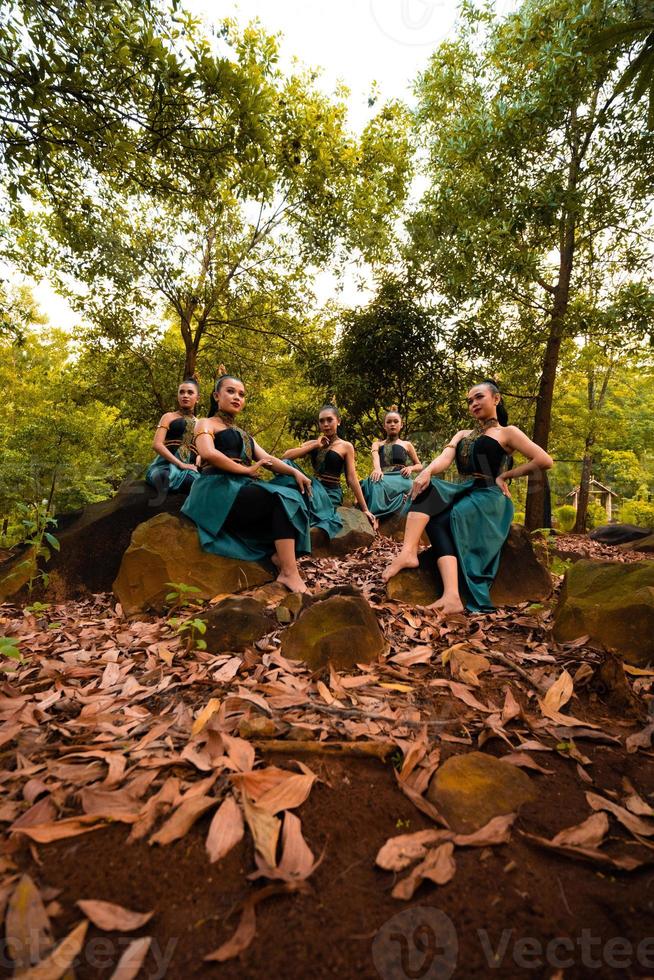 een groep van Aziatisch Dames duurt een vakantie naar de Woud terwijl vervelend een groen rok en zittend Aan een rots foto