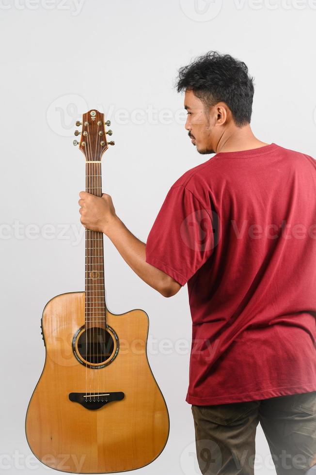 portret van jong Aziatisch Mens in rood t-shirt met een akoestisch gitaar geïsoleerd Aan wit achtergrond foto