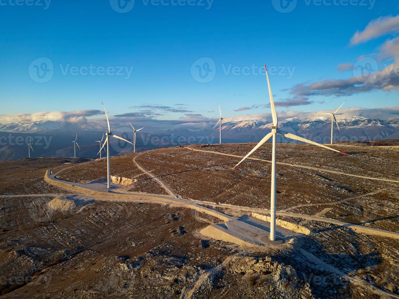 windmolens Aan de heuvels gedurende zonsondergang. hernieuwbaar energie, groen energie. bergen in de achtergrond met sneeuw. wind macht en milieuvriendelijk vriendelijk. duurzame toekomst. einde fossiel brandstoffen. foto