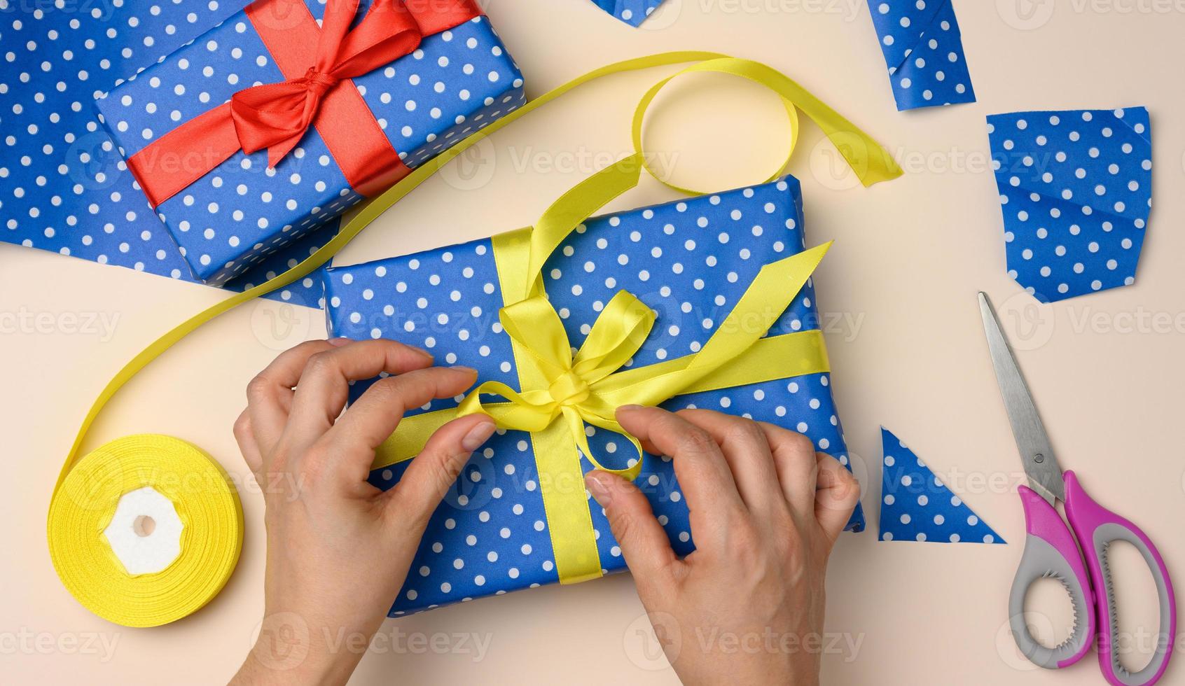 vrouw handen koppelverkoop een geel zijde boog Aan een blauw geschenk doos, voorbereidingen treffen een verrassing foto