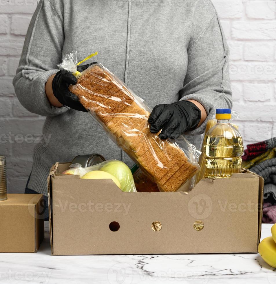 vrouw in een grijs trui is inpakken voedsel in een karton doos, de concept van bijstand en vrijwilligerswerk foto