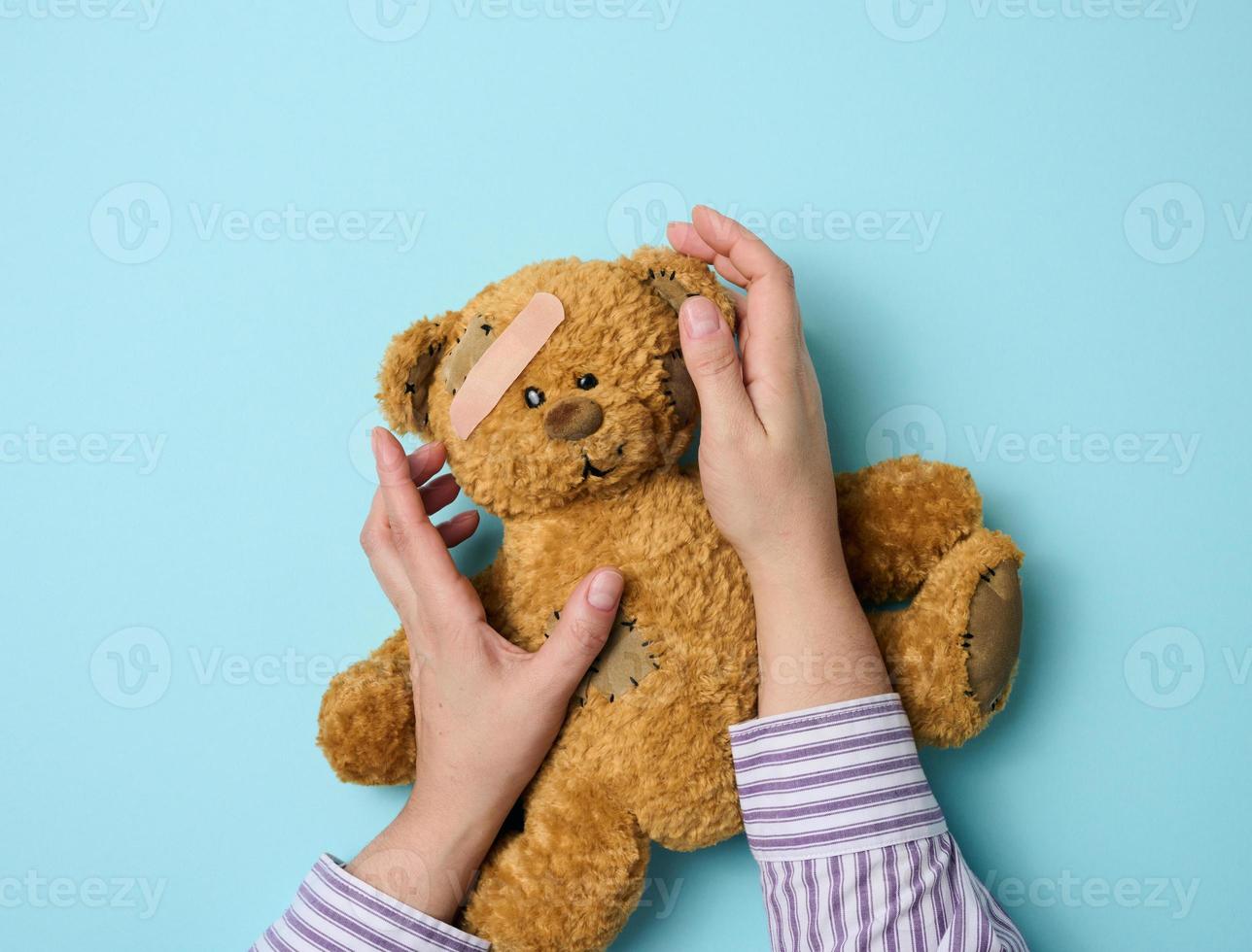 vrouw hand- houdt een bruin teddy beer en lijmen een medisch Zelfklevend gips Aan een blauw achtergrond, tram behandeling foto