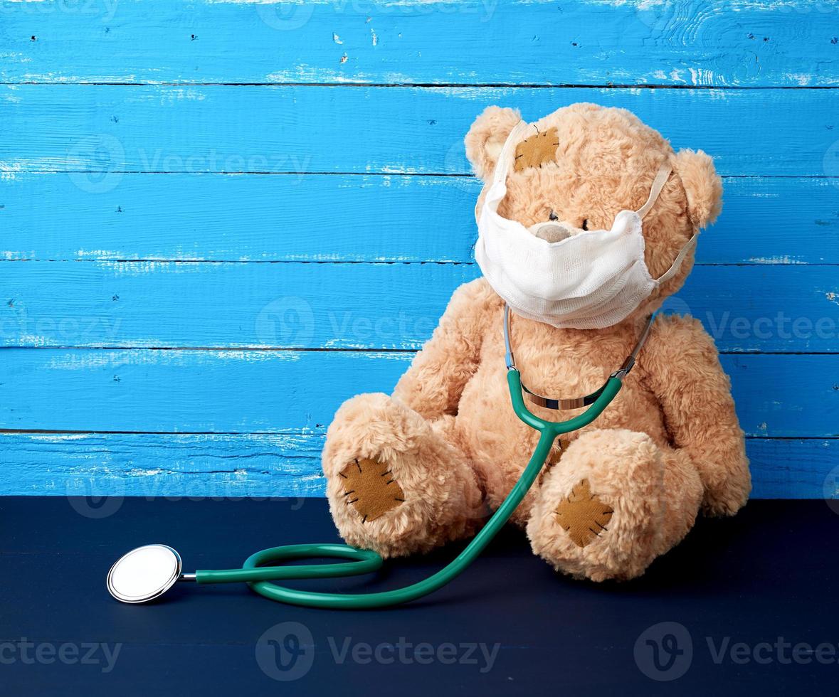 teddy beer is zittend in een wit medisch masker, een groen stethoscoop is hangende Aan zijn nek foto