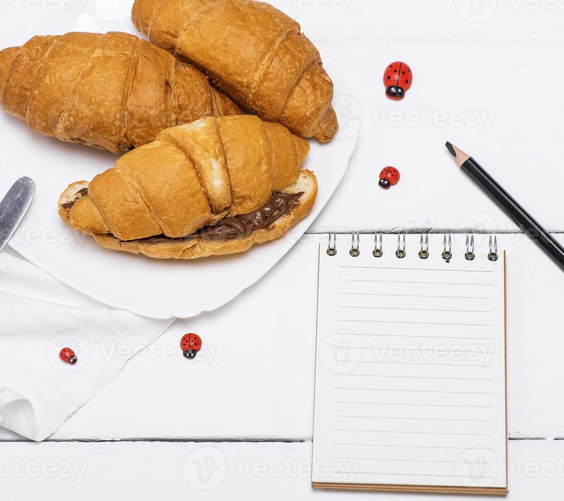 drie gebakken croissants met chocola en een papier kladblok foto