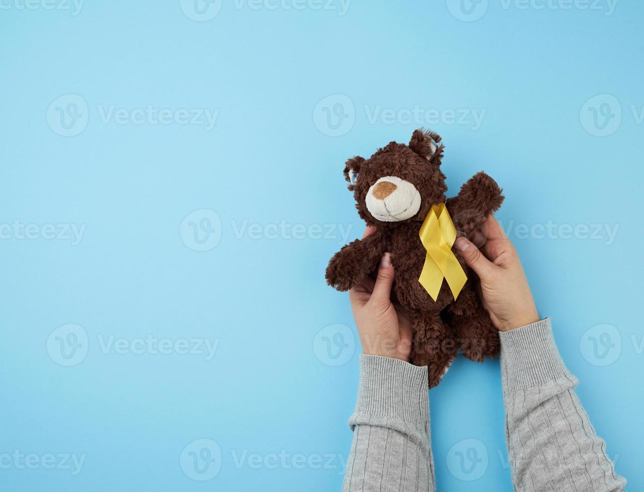 vrouw handen houden een klein bruin teddy beer welke houdt in haar poot een geel lint foto