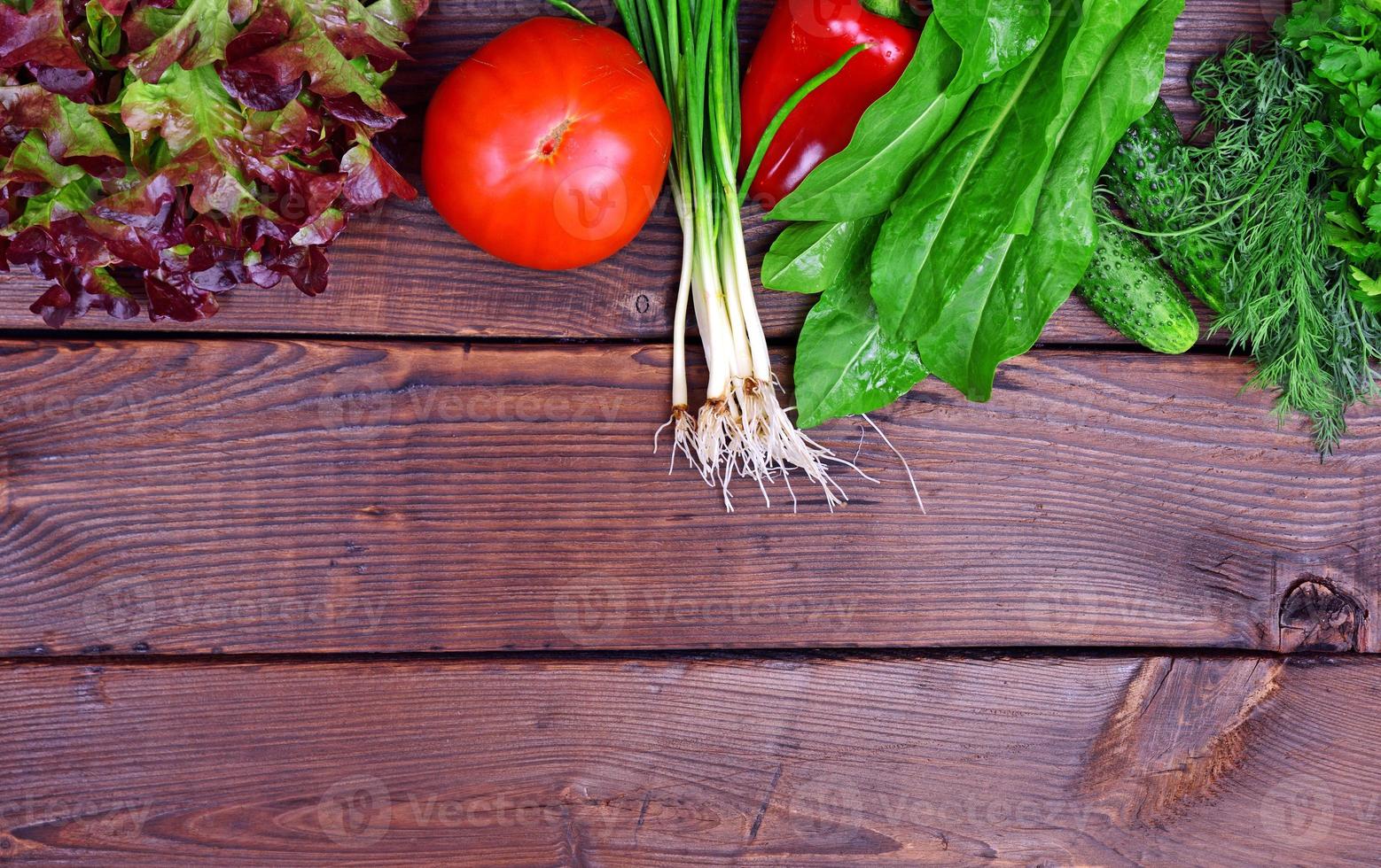 vers tomaat groenten, komkommers en groen uien Aan een bruin houten achtergrond foto