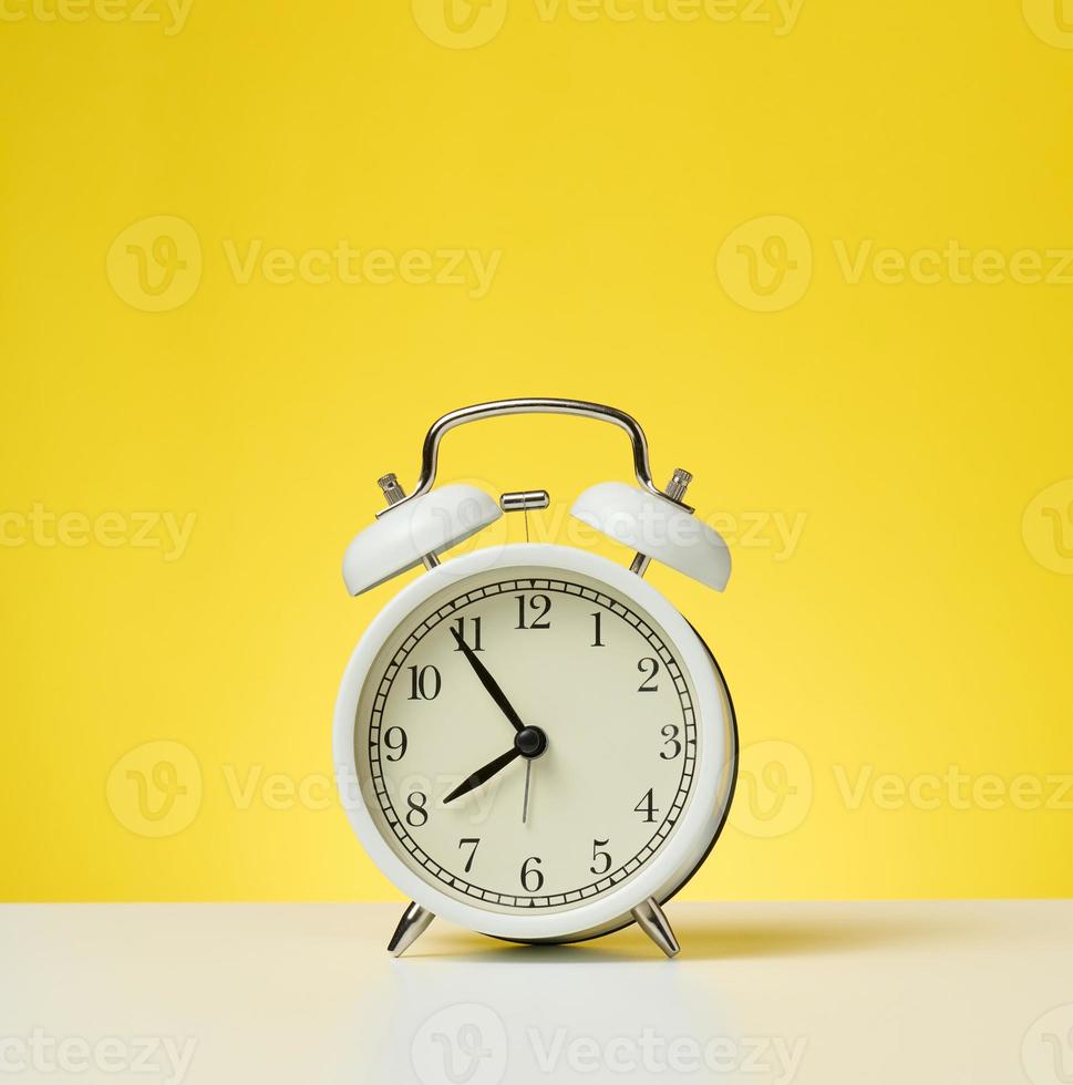 ronde wit alarm klok, vijf minuten naar acht in de ochtend. geel achtergrond foto