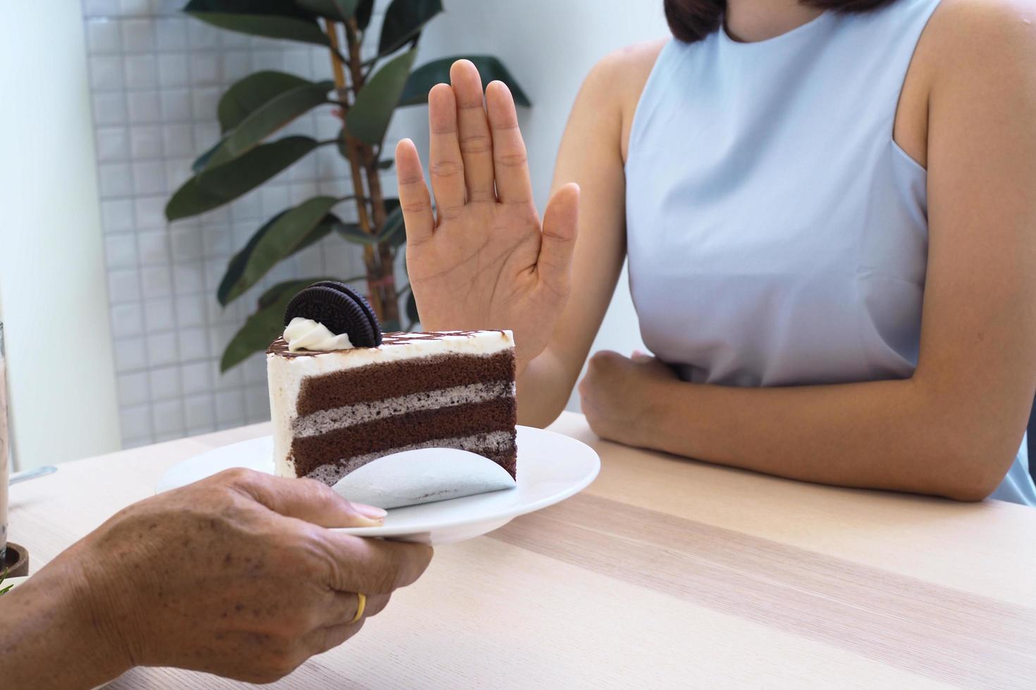 een van de gezondheidszorg meisjes gebruikt een hand- naar Duwen een bord van chocola taart. weigeren naar eten voedingsmiddelen dat bevatten trans dik. foto