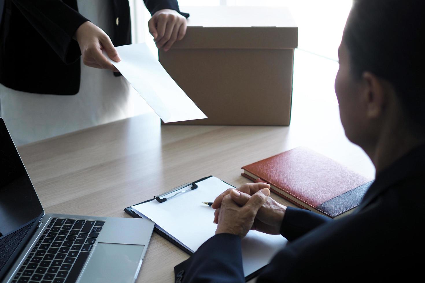 de bedrijf vrouw heeft een bruin karton doos De volgende naar haar lichaam en stuurt een brief van ontslag naar de leidinggevend. omvatten over ontslag, baan plaatsing en vacatures. foto