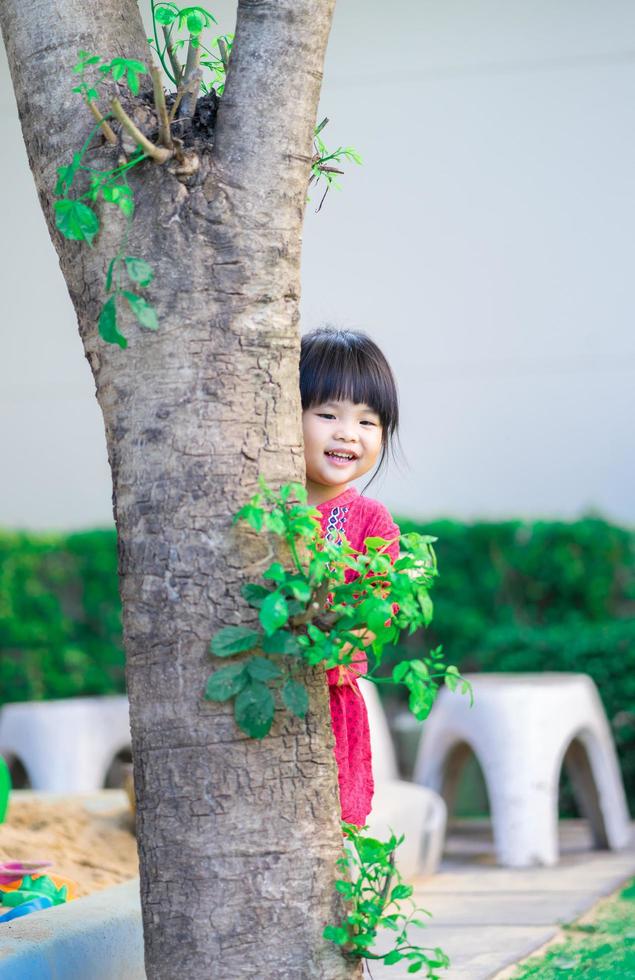klein meisje sluipen achter de boom in het park foto