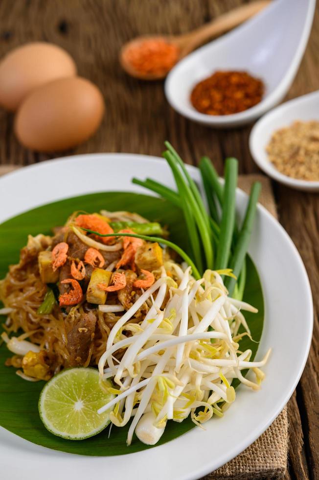 pad thai met citroen, eieren en kruiden op een houten tafel foto