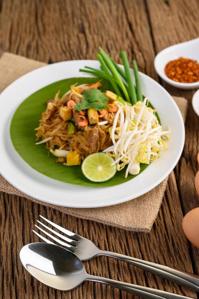 pad thai met citroen, eieren en kruiden op een houten tafel foto