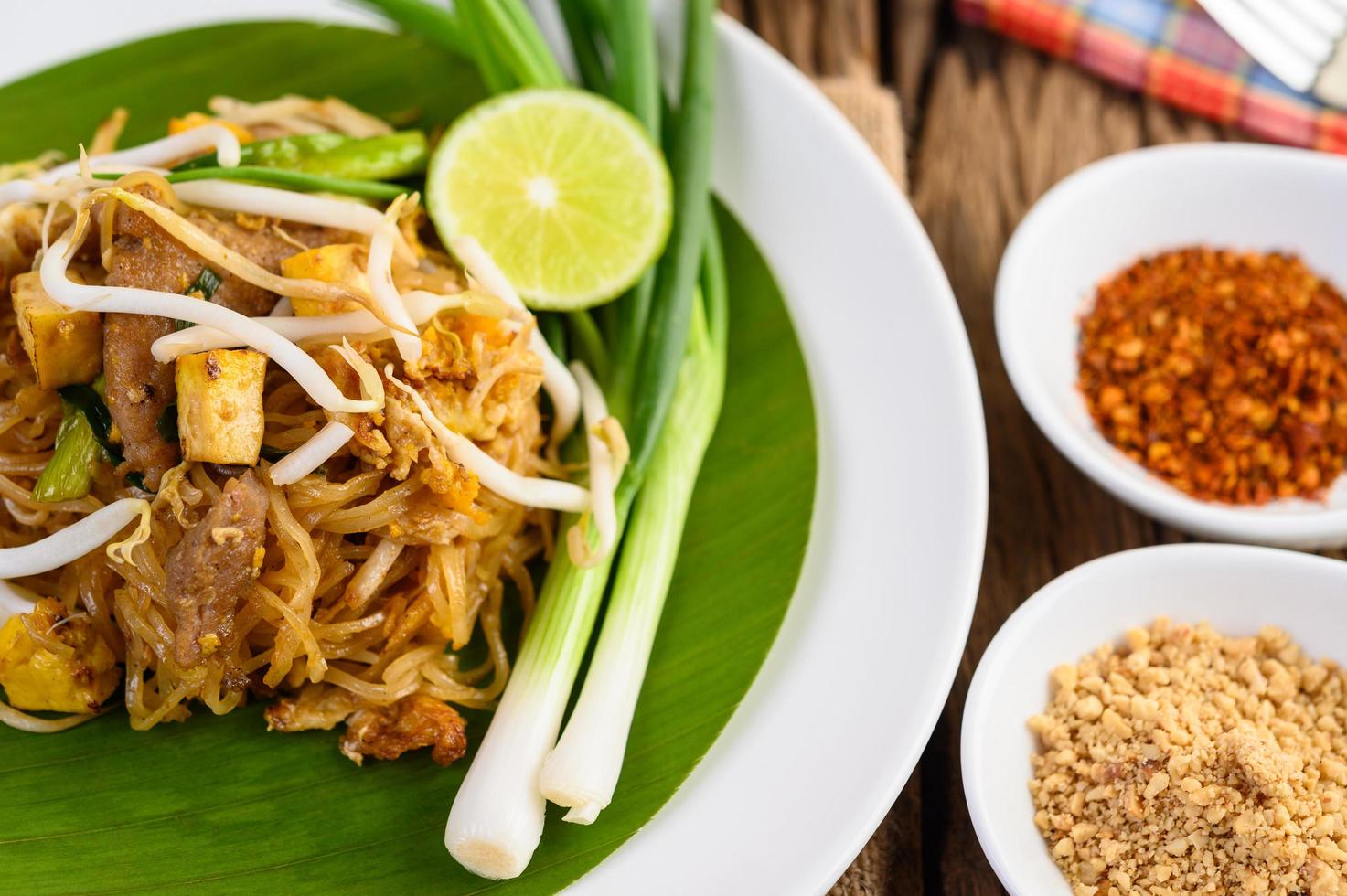 pad thai met citroen, eieren en kruiden op een houten tafel foto