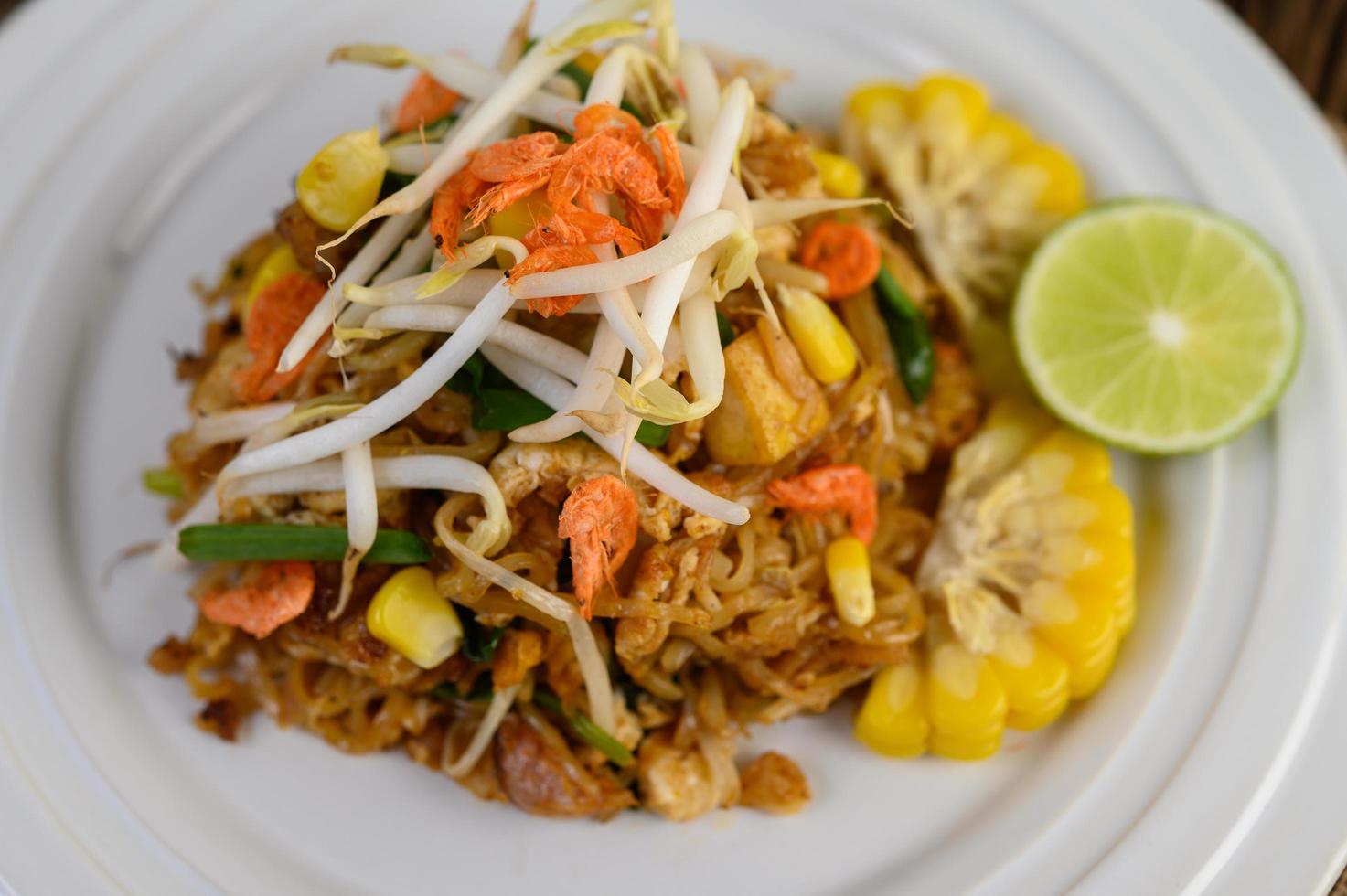 pad thai met citroen, eieren en kruiden op een houten tafel foto