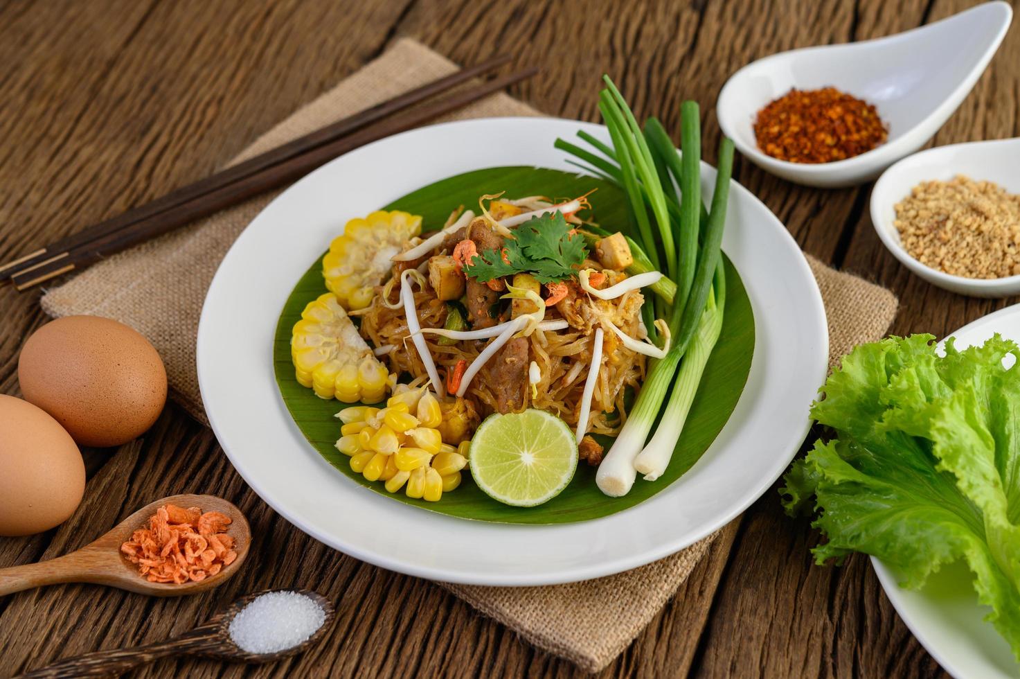 pad thai met citroen, eieren en kruiden op een houten tafel foto