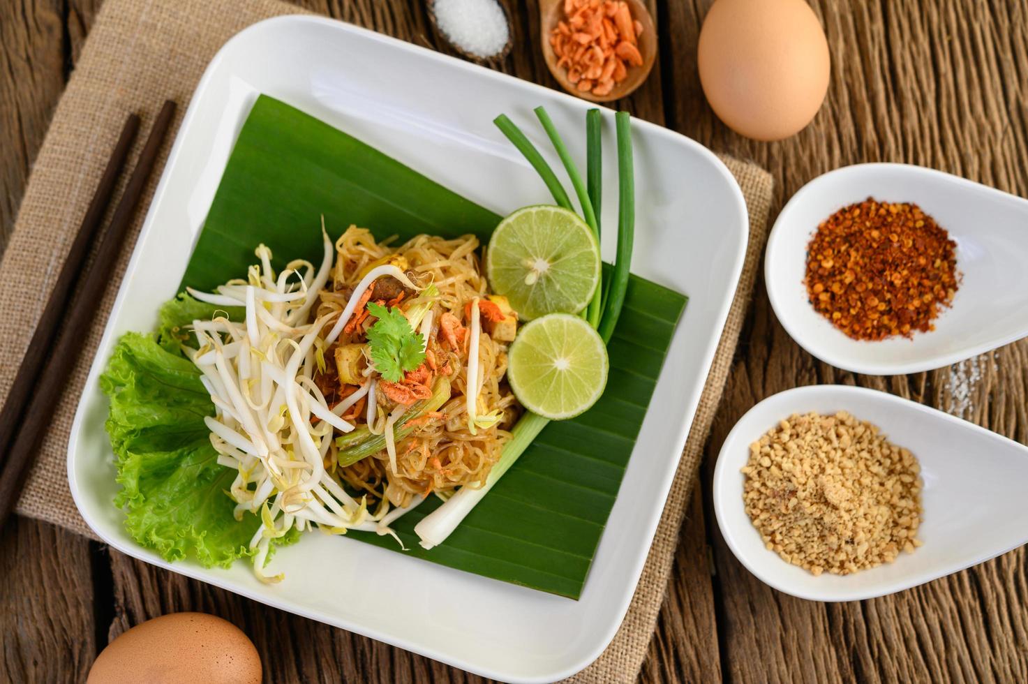 pad thai met citroen, eieren en kruiden op een houten tafel foto