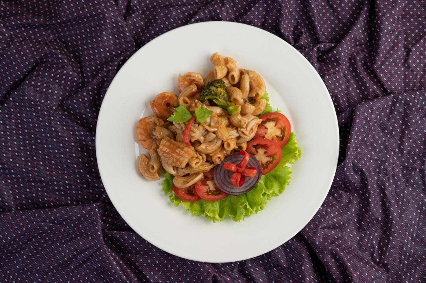 geroerde garnalenmacaroni op een witte plaat met tomaten en salade foto