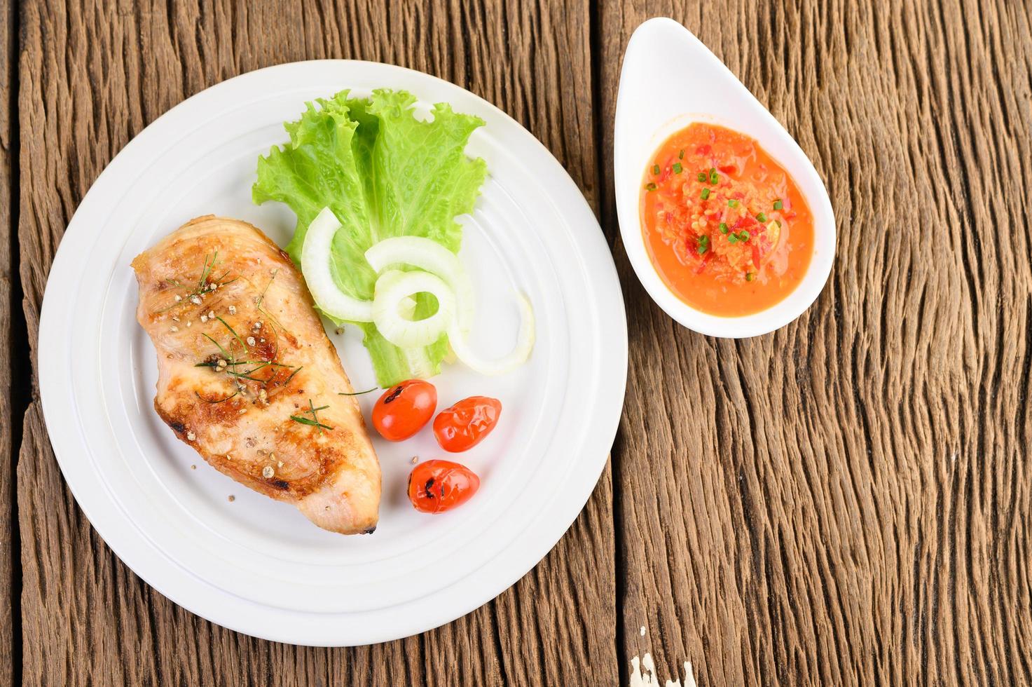 gegrilde kip op een houten tafel met tomaten, salade, ui en chilisaus foto