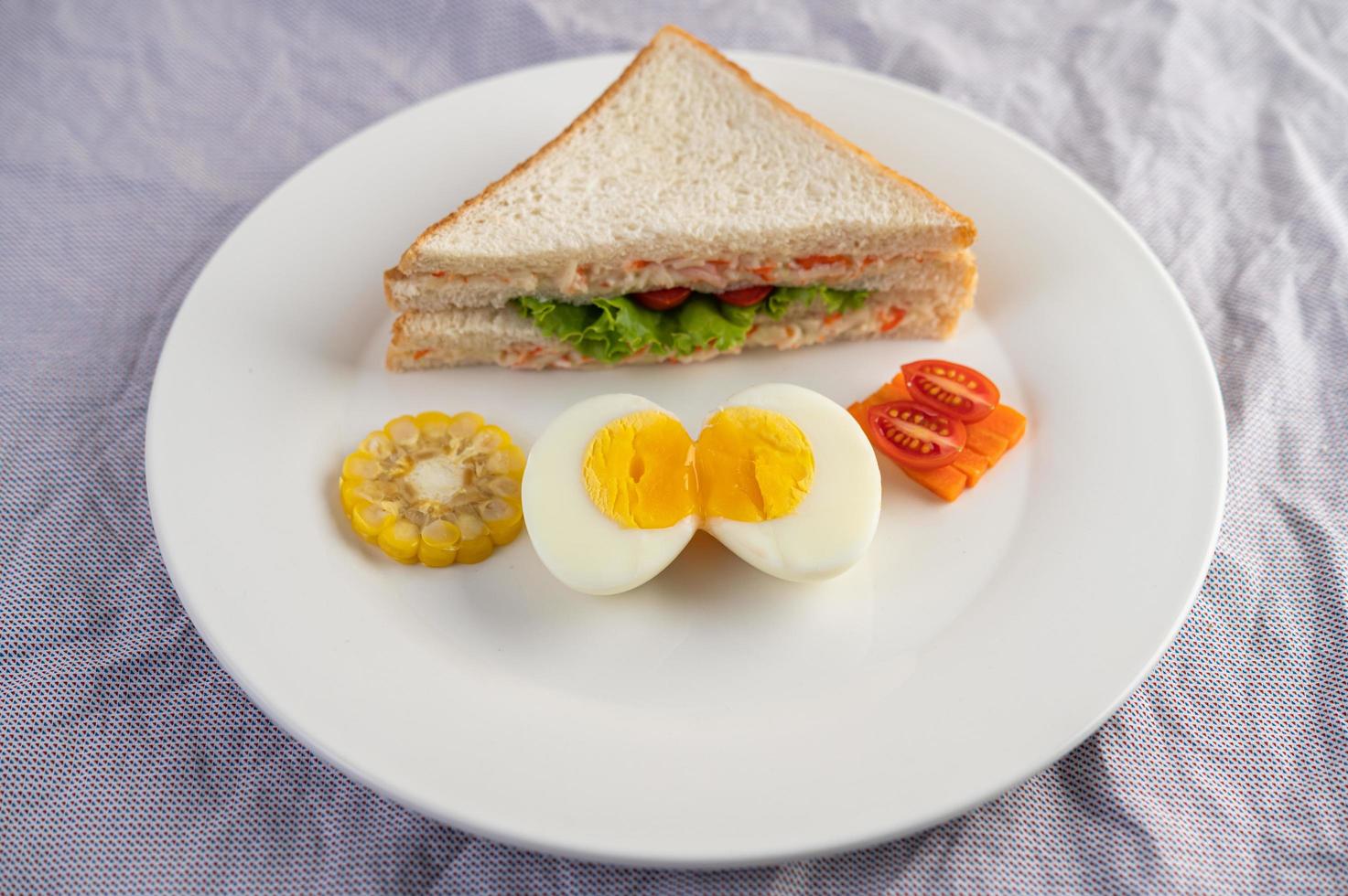 gekookte eieren, maïs, tomatensandwich op een witte plaat foto