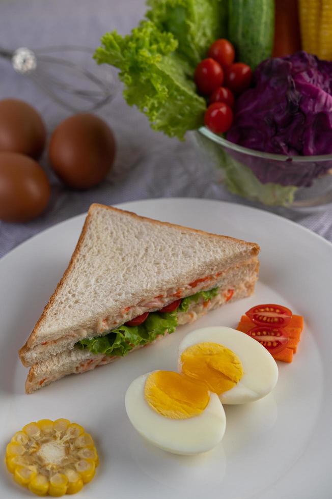 gekookte eieren, maïs, tomatensandwich op een witte plaat foto
