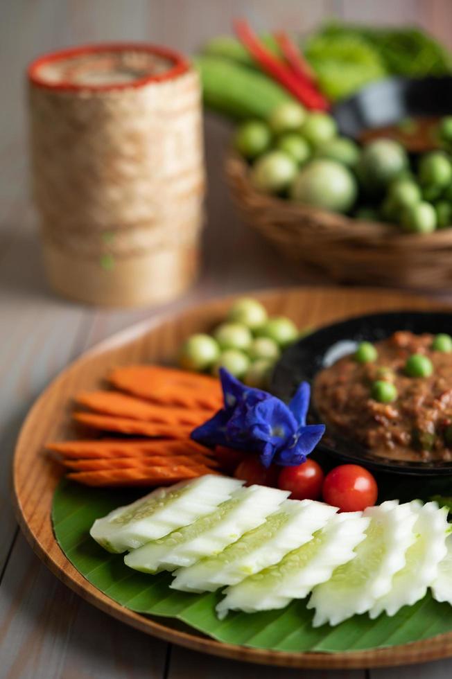 chilipasta in een kom met aubergine, wortelen, chili en komkommers in een mandje foto