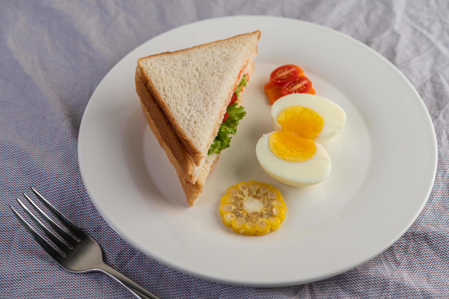 gekookte eieren, maïs, tomatensandwich op een witte plaat foto