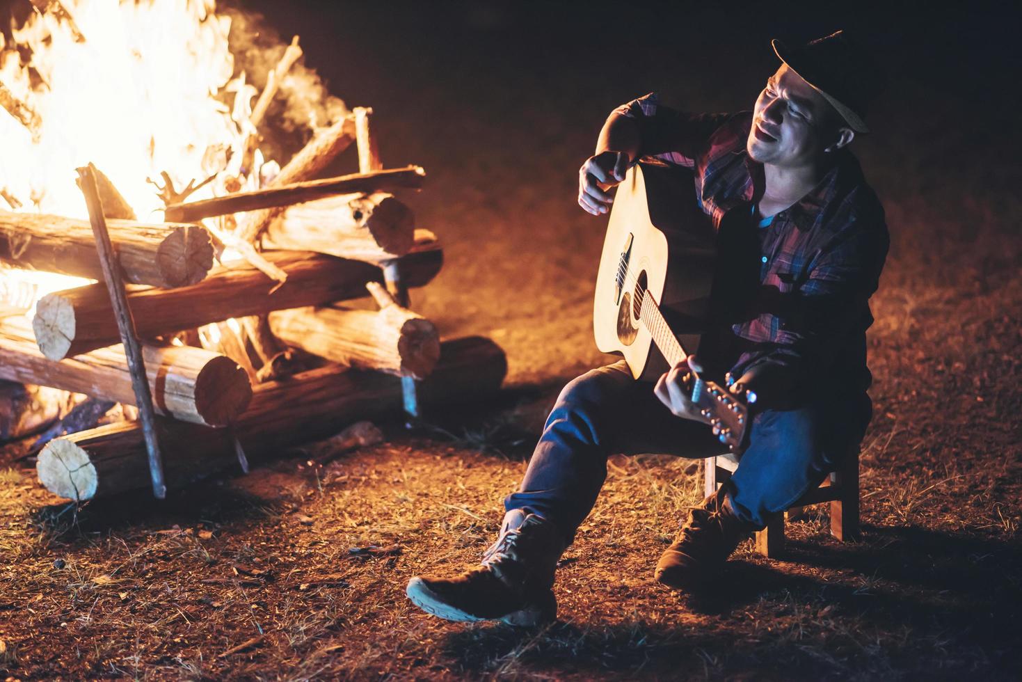 jonge man zit rond het kampvuur gitaar spelen foto