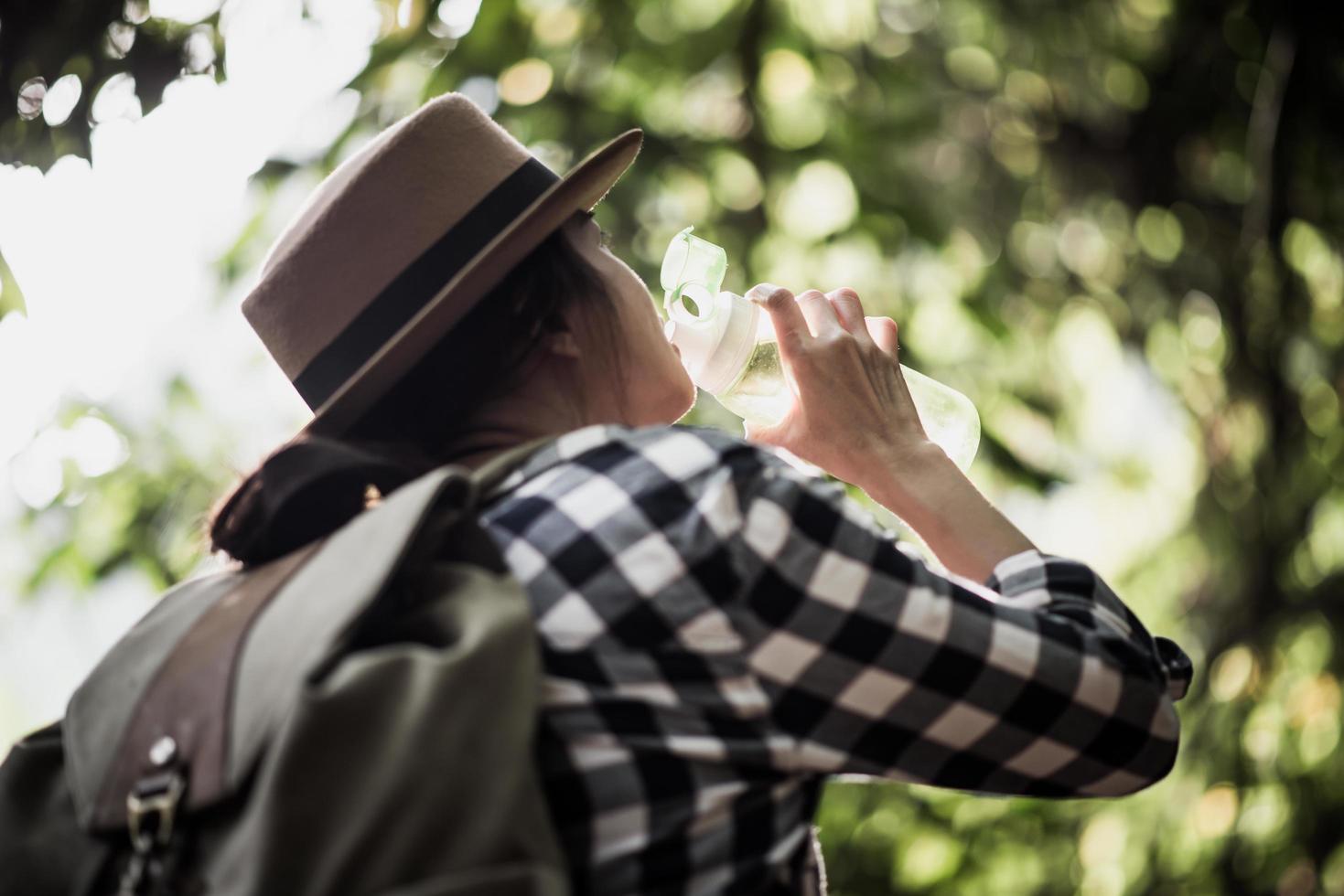 jonge vrouw drinkwater tijdens het reizen in het bos foto