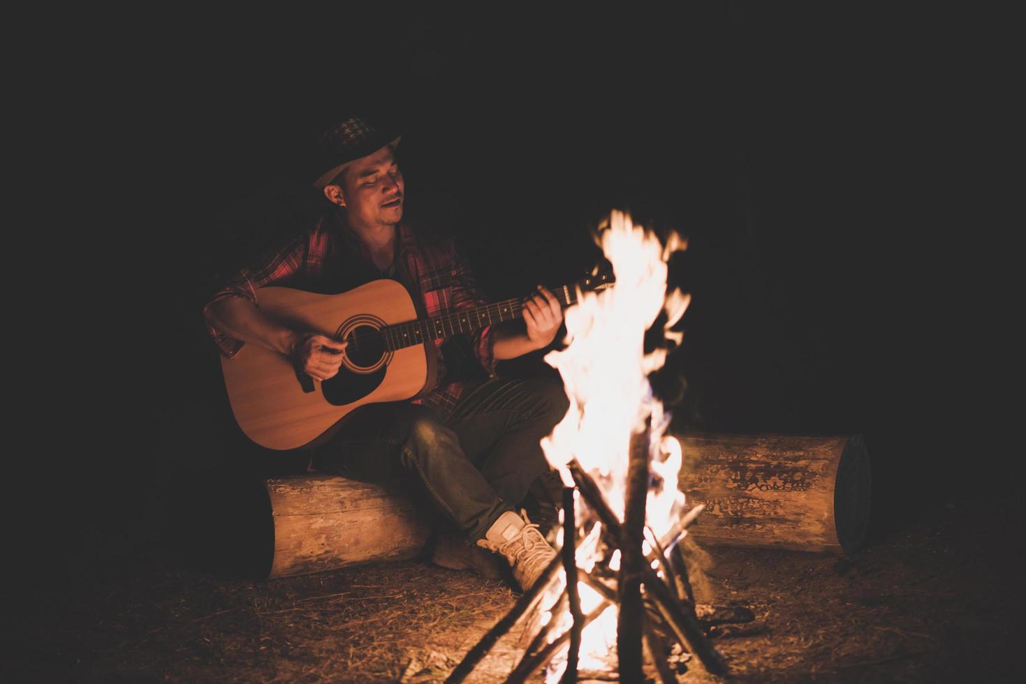 jonge man zit rond het kampvuur gitaar spelen foto