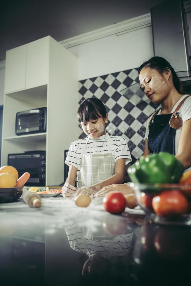 schattig klein meisje en moeder in schorten die deeg in huiskeuken afvlakken foto